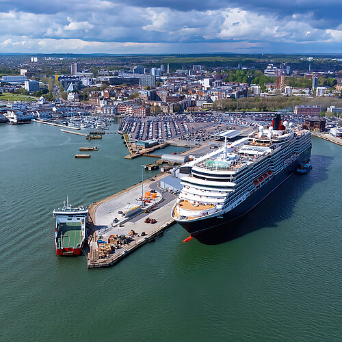 Cruise ship and ferry at Southampton Harbour, city in the background under cloudy skies.